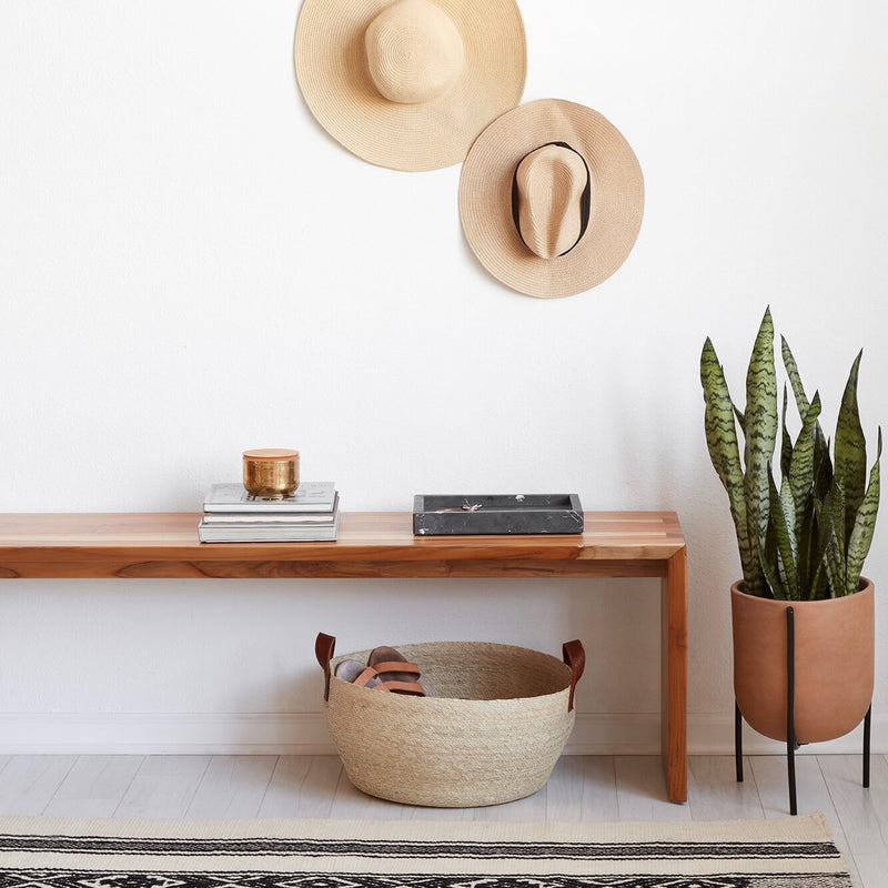 Handwoven palm storage basket under entryway bench, natural