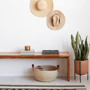 Handwoven palm storage basket under entryway bench, natural