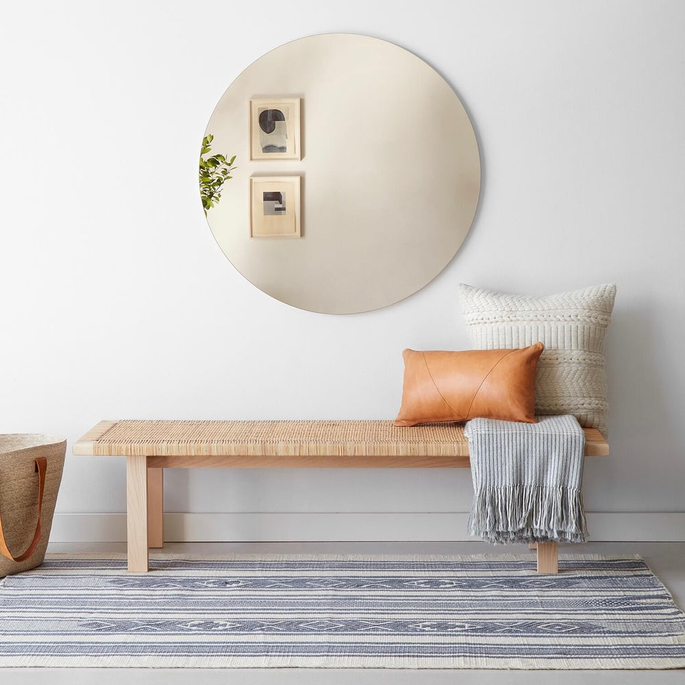 Large circular mirror above bench with throw pillow
