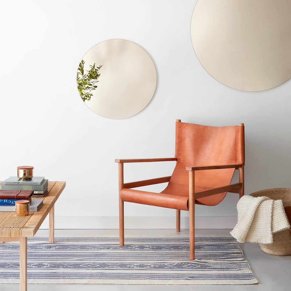 Small and large circular mirror on wall above leather chair