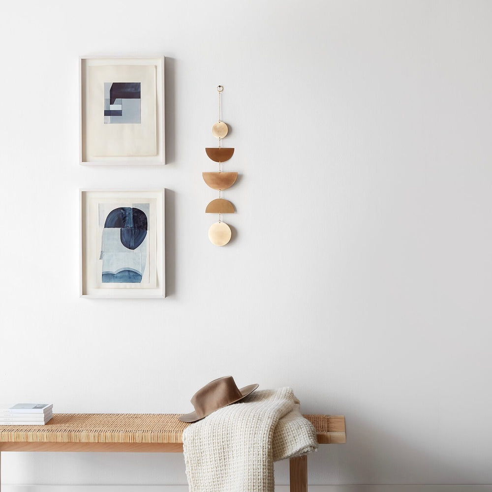 Geometric brass wall hanging in gallery arrangement with abstract art above a woven bench