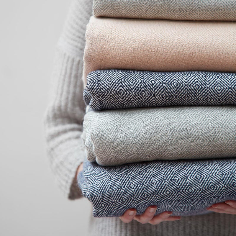 woman holding stack of alpaca throw blankets, dove-grey
