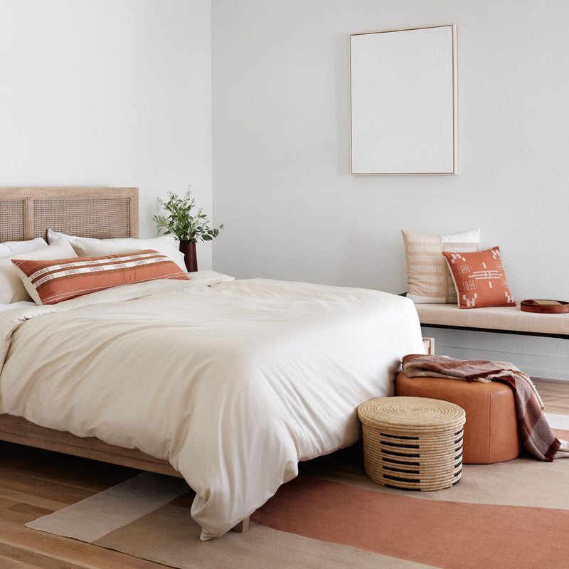 Lumbar pillow styled on bed with area rug and floor baskets, solid-sand