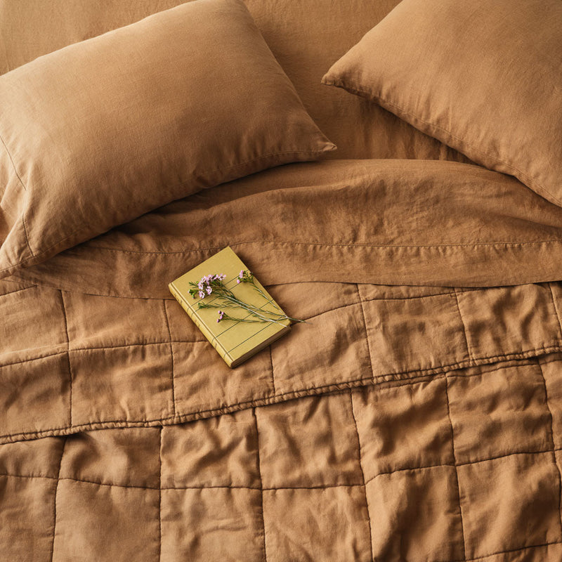 Overhead of linen sheet set and quilt, camel