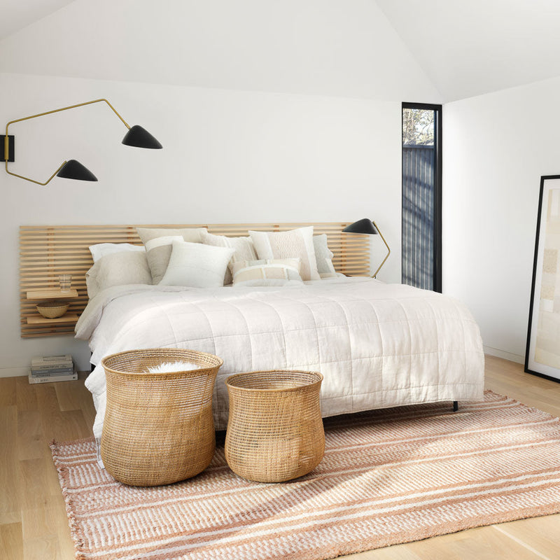 Woven baskets at foot of styled bed with sand striped linen quilt, sand-stripe