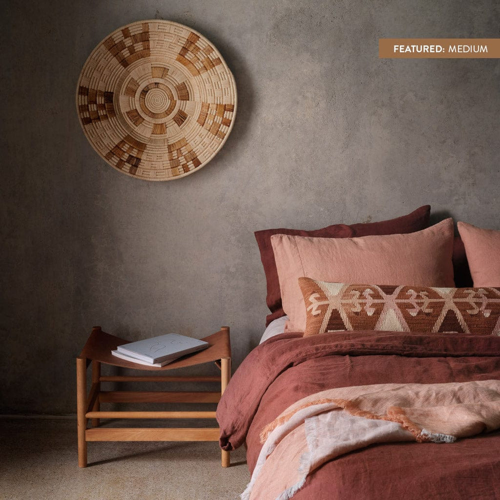 Zomba medium woven wall hanging over stool next to bed with rose linen bedding