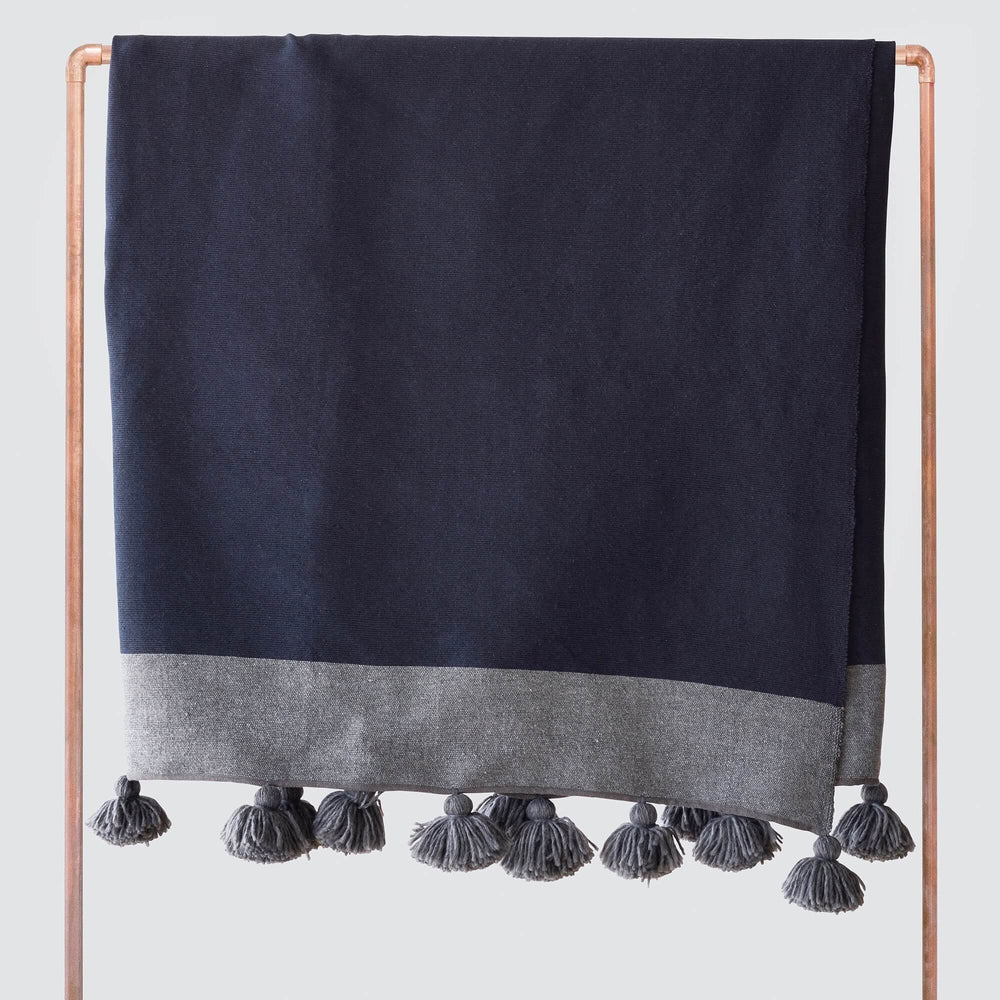 Navy and grey cotton throw with oversized tassels draped over copper rack